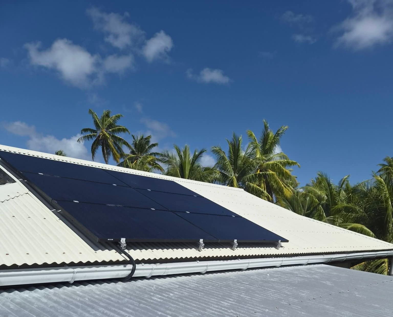 Panneaux photovoltaïques sur une toiture face au lagon, entourés de cocotiers